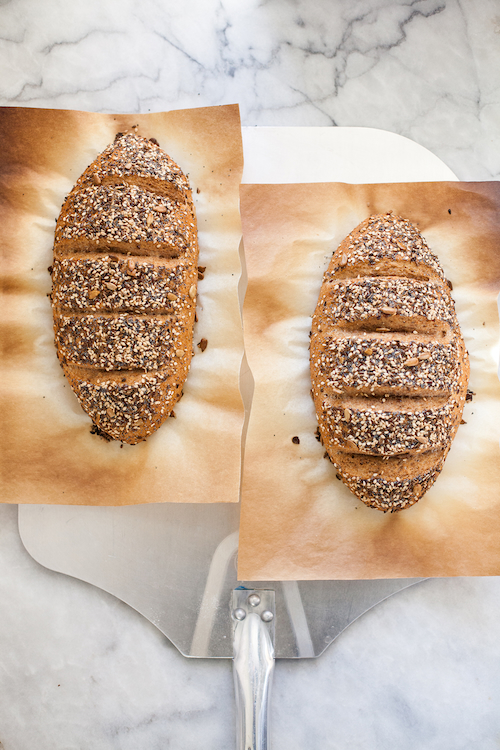 two loaves of bread on parchment paper on a peel